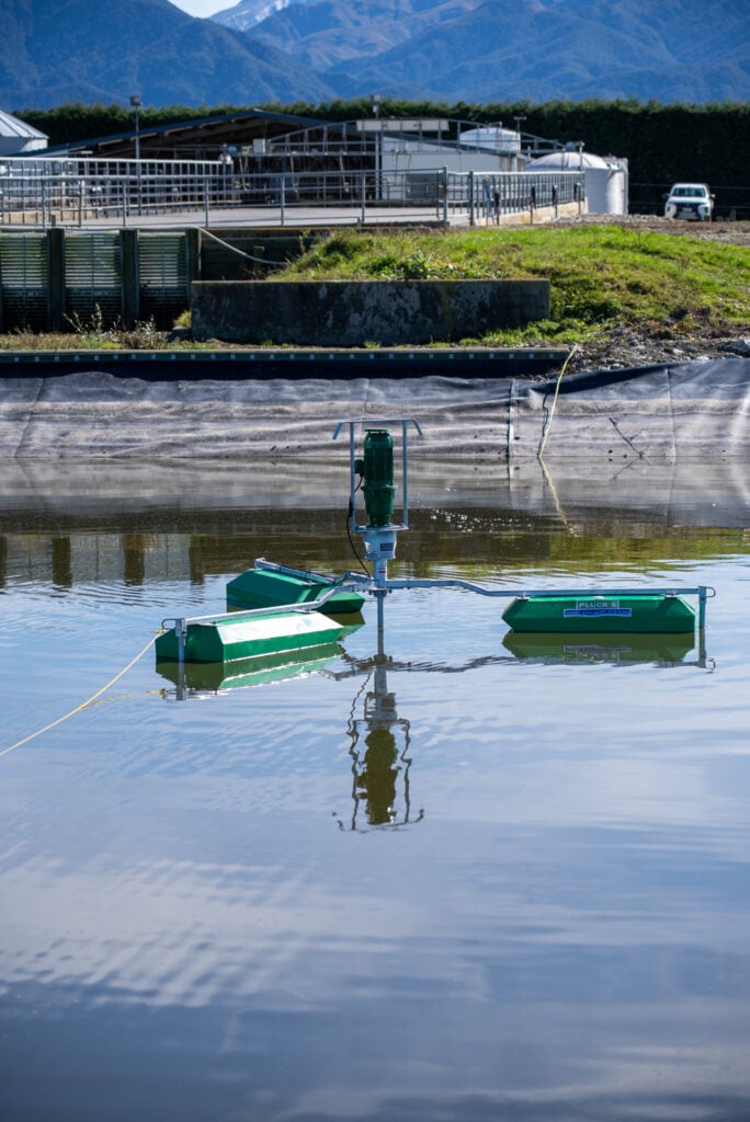 DSC00218 Plucks Engineering effluent pond stirrer operating in a dairy farm effluent storage pond, with dairy shed infrastructure and Southern Alps visible in the background