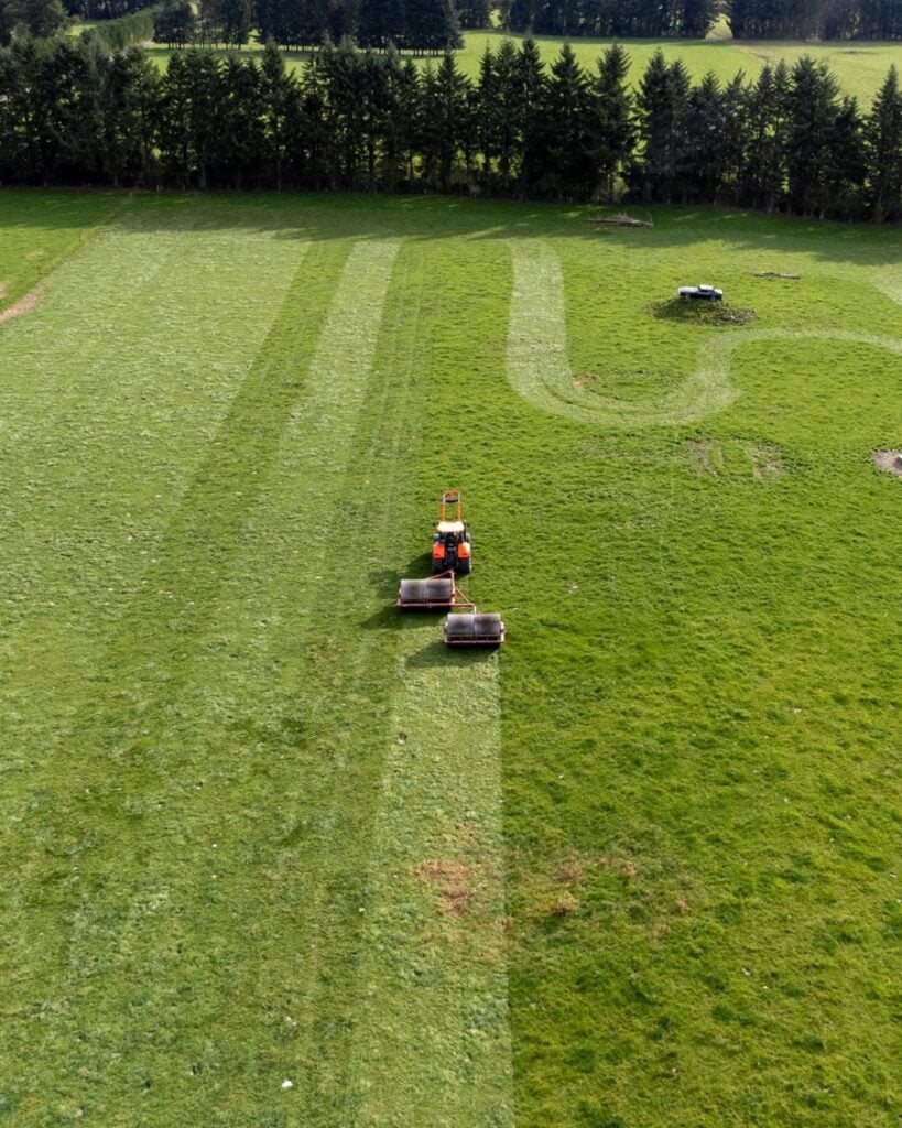 Aerial view of a tractor towing a Plucks double land roller setup across a Canterbury paddock, with rolled stripes visible in the pasture
