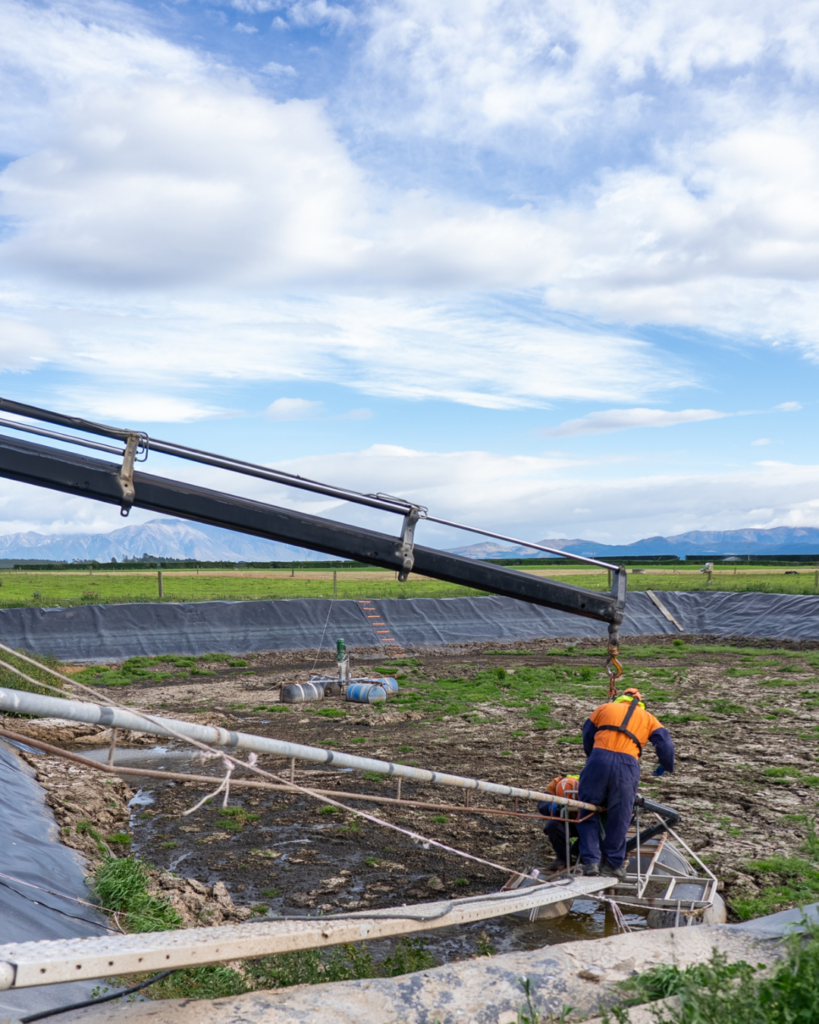 Plucks Engineering SM Posts Two Plucks Engineering technicians installing an effluent stirrer frame at a Canterbury dairy farm pond, with the Southern Alps in the background.