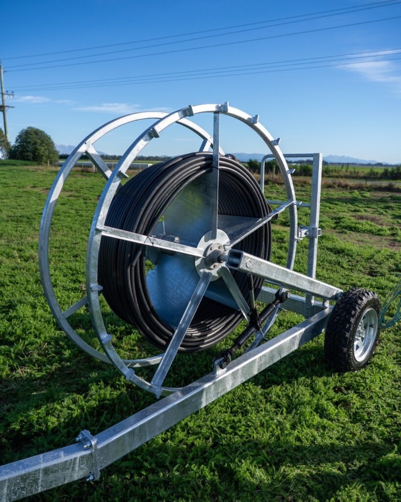 Plucks Hose Runner on a wheeled galvanised frame, wound with black alkathene stock water hose in a paddock