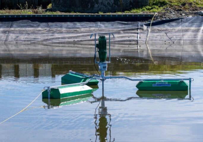 DSC00218 Plucks Engineering effluent pond stirrer operating in a dairy farm effluent storage pond, with dairy shed infrastructure and Southern Alps visible in the background