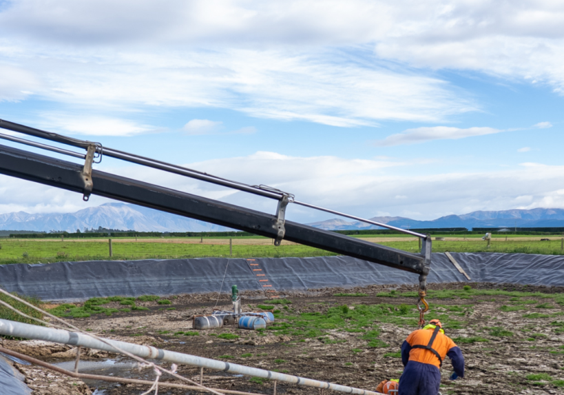 Plucks Engineering SM Posts Two Plucks Engineering technicians installing an effluent stirrer frame at a Canterbury dairy farm pond, with the Southern Alps in the background.