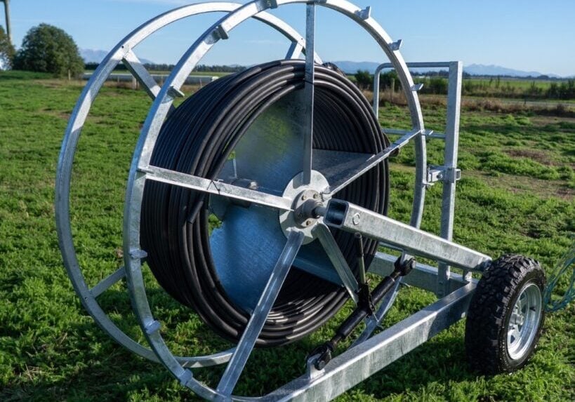 plucks-hose-runner-alkathene-hose Plucks Hose Runner on a wheeled galvanised frame, wound with black alkathene stock water hose in a paddock